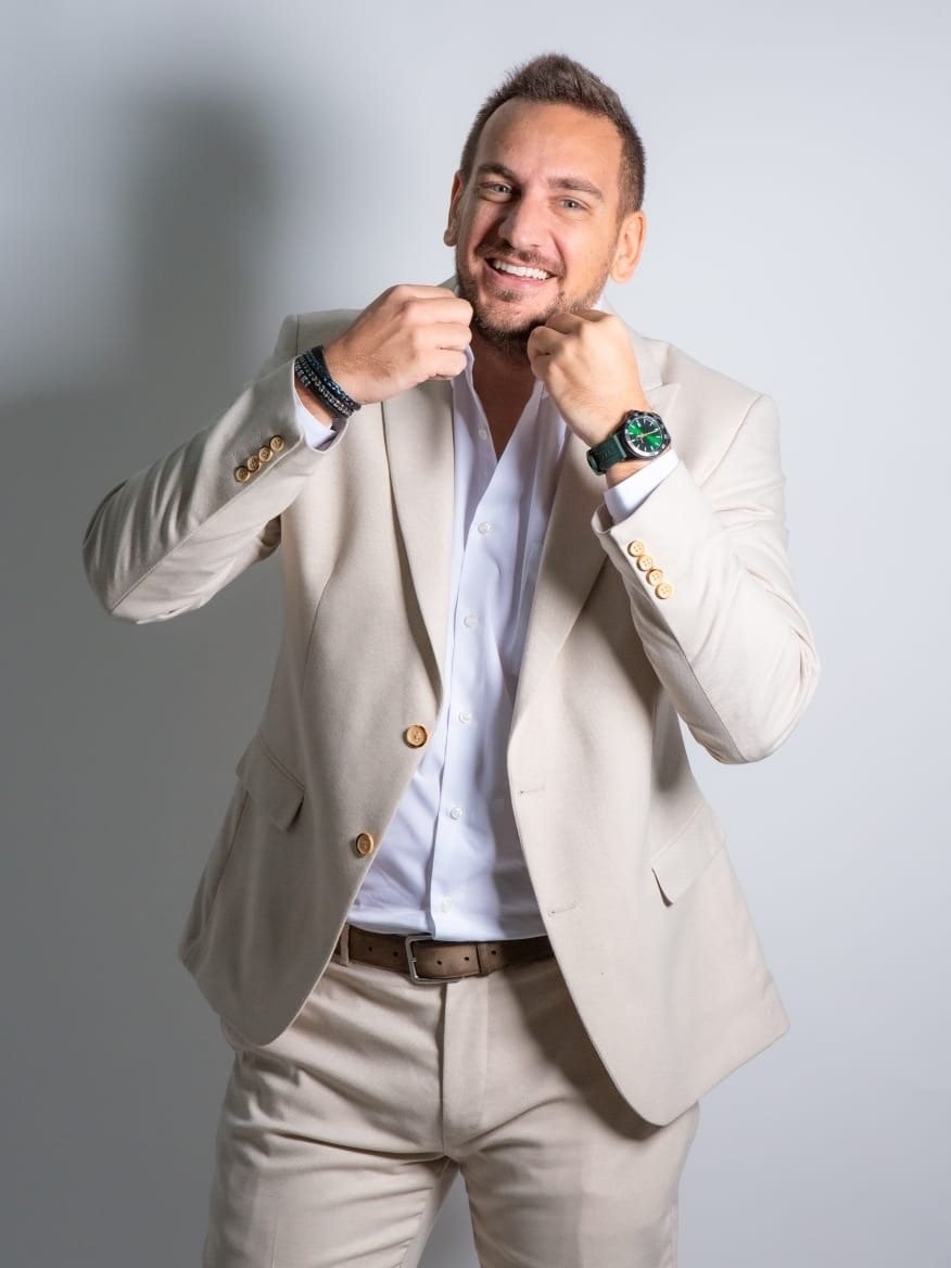 Riad Al Chami in an ivory suit, smiling, fists raised in a playful boxer's pose